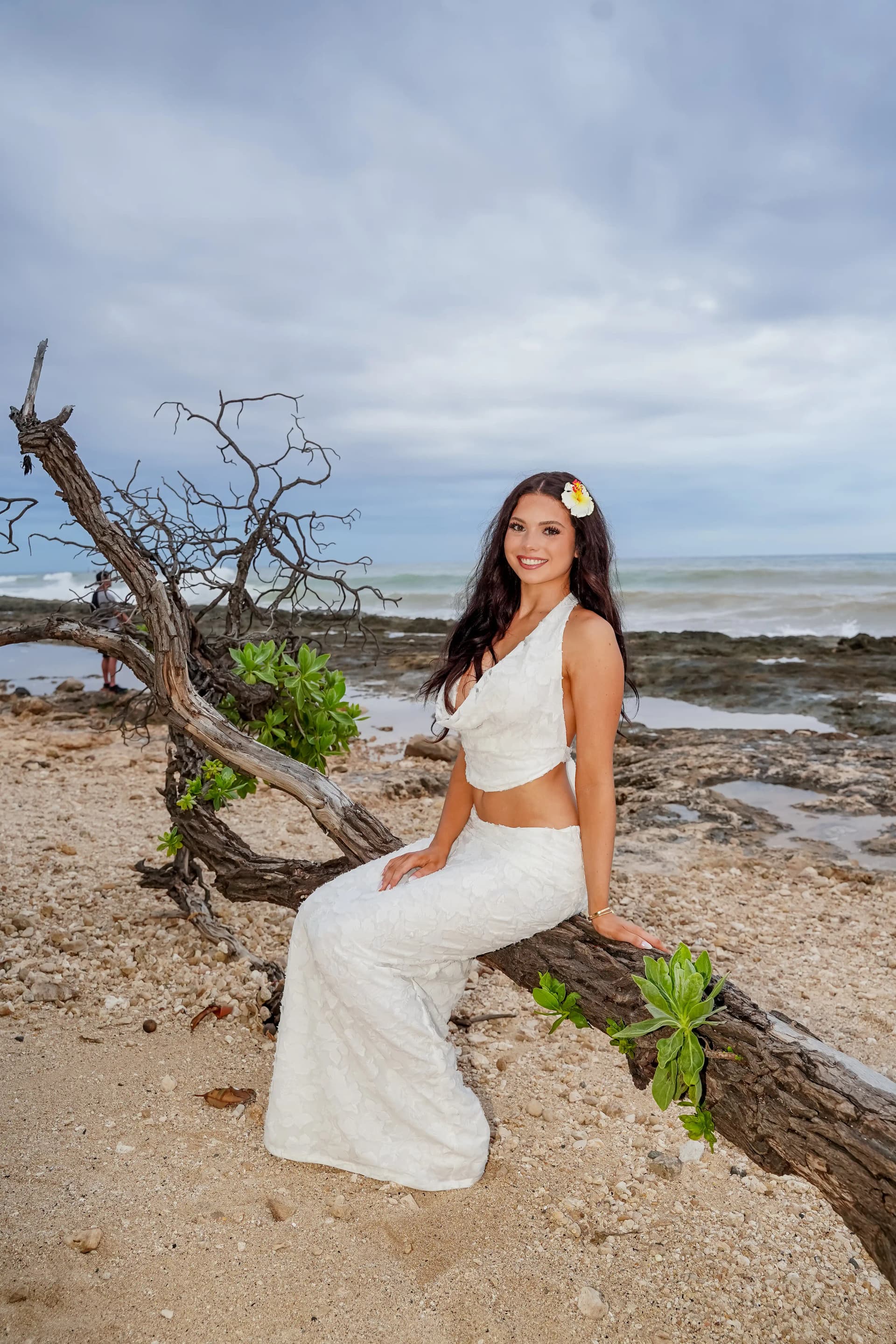 Solo female portrait seated on driftwood by the ocean